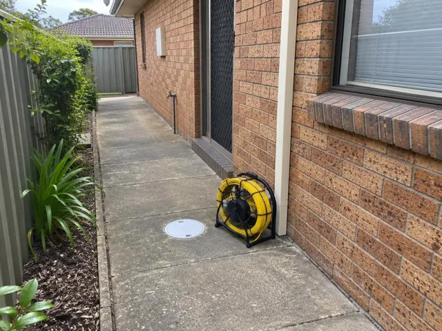 Brick side passage with a capped inspection opening and coiled reel beside the house in Doonside